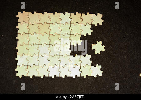 Half ordered puzzle with white jigsaw pieces. One side of the image shows part of the completed puzzle, other side shows the work in progress on a tex Stock Photo