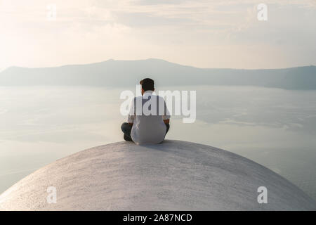 31th Oct 2019 - Santorini, Greece. A man enjoys a peaceful view of an Agean sea on the roof of a building in Fira town, capital of Santorini. Stock Photo