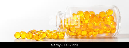 Yellow pill capsules crumble from a glass bottle on a white background Stock Photo