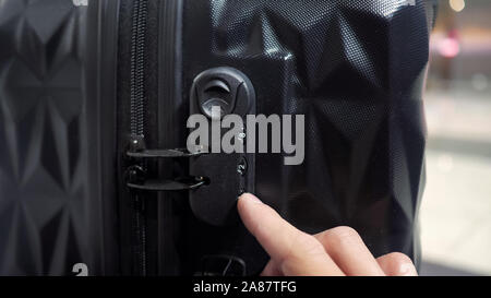 man enters the code to open suitcase combination lock on the suitcase and presses the button, hands closeup. Stock Photo