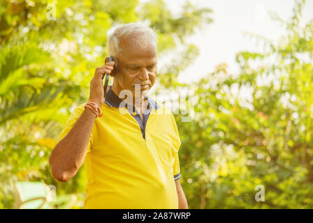 Elder man busy in mobile - Healthy senior Indian on phone outdoor at park, Morning - Happy male parent talking on phone. Stock Photo