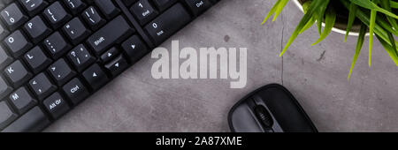 Working place on dark table with copy space. Table with keyboard, computer mouse, flower in pot. Flat lay. Top view, the sun's rays from the side Stock Photo