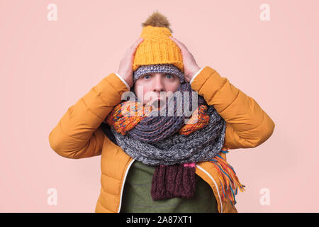 Handsome caucasian shocked funny man in several hats and scarfs being surprised on pink background. Winter fashion. Stock Photo