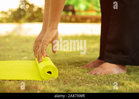 Practicing yoga or pilates outdoors - Senior man hands preparing yoga mat at park - close up, getting ready to do yoga on mat. Stock Photo
