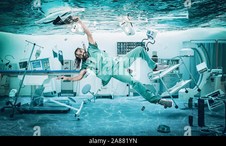 Smiling doctor floats under water in a flooded operating room. problems at work and in the medical field. Stock Photo