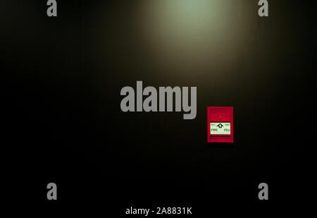 Red fire alarm pull station on black wall background. Fire alarm switch. Emergency safety system. Fire alarm on dark concrete wall. Warning Stock Photo