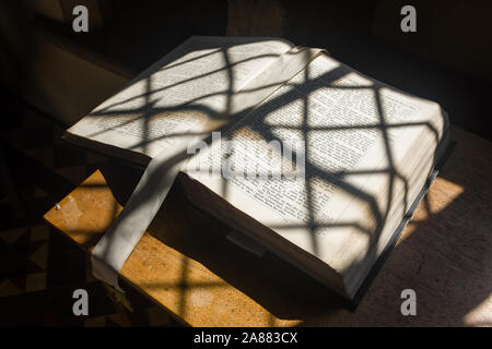 An open bible in a parish church, shadows from a stained glass window forming a pattern on the open pages; England, UK Stock Photo