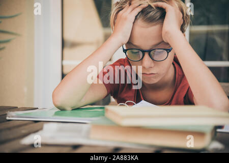 Tired student doing homework at home sitting outdoor with school books and newspaper. Boy weary due to heavy study. Kid asleep on the copybook after l Stock Photo