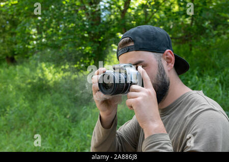 The camera smokes in the hands of a photographer takes a photo in nature. young bearded man photographs outdoors. Stock Photo