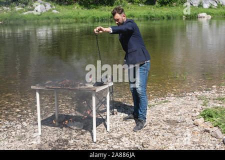 Frustrated male office worker hate his job. young bearded guy, hipster in jacket set fire to desk and chair, destroyed his workplace. Stock Photo