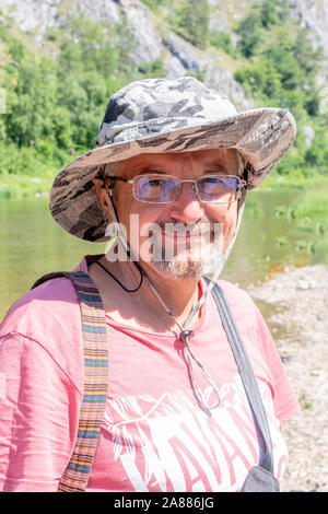 portrait of an intelligent elderly man wearing glasses. bearded hoary old man in a hat smiles against the background of park in outdoor. Middle age se Stock Photo