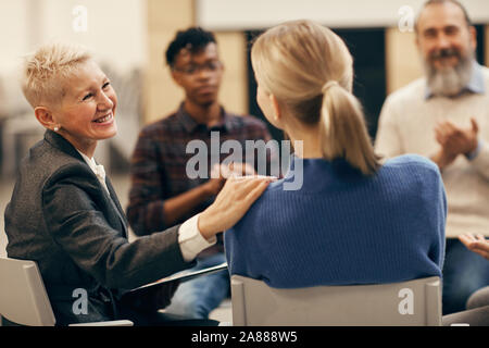 Smiling mature woman with short hair talking to the young woman during therapy lesson Stock Photo