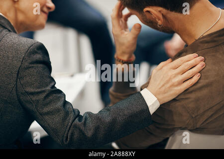 Rear view of mature woman supporting young man she touching his shoulder while they sitting on chair Stock Photo