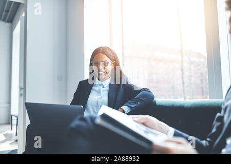 Smiling African American businesswoman working on a laptop during a meeting with colleagues in an office Stock Photo