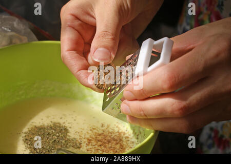 The girl rubs a nutmeg on a fine grater in a bowl with dough. The process of making cream sauce with a nutty nut. Hands and a small grater over a bowl Stock Photo