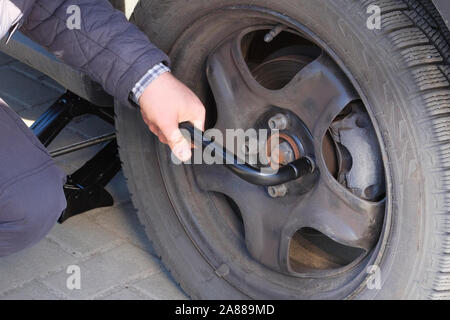 Driver is screwing and unscrewing changing car wheel by wrench. Damaged car tyre. Change a flat car tire on road. Auto repair concept. Stock Photo
