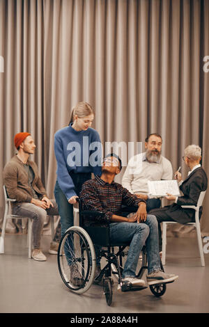 Young woman standing and talking to the African young man with disability during therapy lesson Stock Photo
