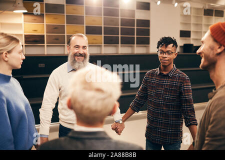 Multiethnic group of people standing in circle holding hands and doing relaxation exercise during therapy lesson Stock Photo