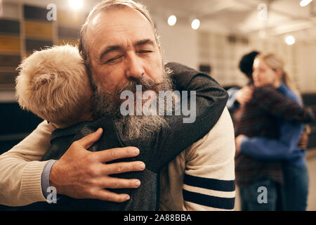Senior bearded man embracing woman and enjoying the hug during therapy with other couple in the background Stock Photo