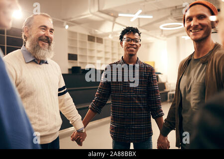 Group of happy people standing holding hands and smiling to each other during business training at office Stock Photo