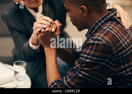 Close-up of mature woman holding hands with her patient and giving him some advice to solve his problem Stock Photo
