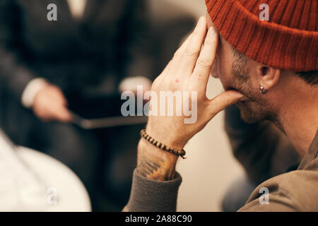 Rear view of young man in hat thinking about something while sitting at meeting Stock Photo