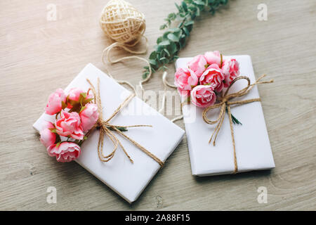 Handmade present box wrapped in paper with branch of roses. Eucalyptus branch and rustic hemp cord spools on background Stock Photo