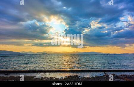 Beautiful sunset with the sun behind colorful clouds over the Aegan sea in Aegina island in Greece -- Panoramic sundown seascape - landscape Stock Photo