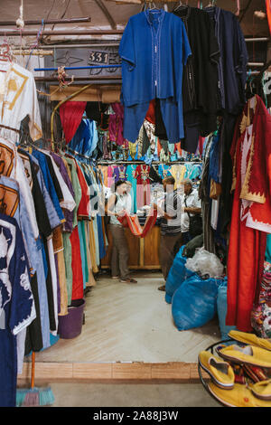Rissani, Morocco - September 18th, 2019: Textile shop and man and woman talking about clothes prices in Rissani bazaar market, in Morocco. Stock Photo