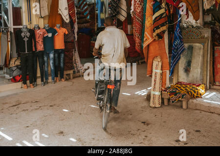 Rissani, Morocco - September 18th, 2019: Man crossing a corridor by bicycle in Risanni bazaar market in Morocco. Stock Photo