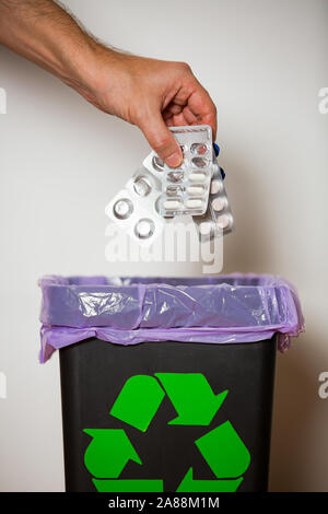 Hand putting expired medicine packages into bin with recycling sign for safe disposal. Person separating dangerous waste. Medical waste management Stock Photo