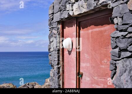 White worker helmet hanging on an old wooden door of a stone house (Achadas Da Cruz, Madeira, Portugal, Europe) Stock Photo