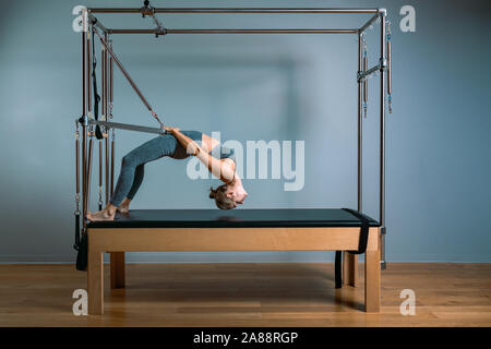 Pilates woman in a Cadillac reformer doing stretching exercises in