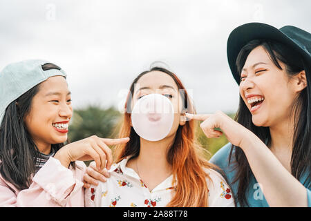 Happy Asian friends having fun with chewing bubble gum outdoor - Young people playing and laughing together Stock Photo