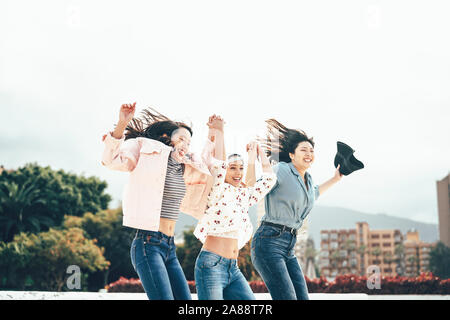 Happy Asian girls jumping together outdoor - Young women friends having fun during university break dancing and celebrating outside Stock Photo