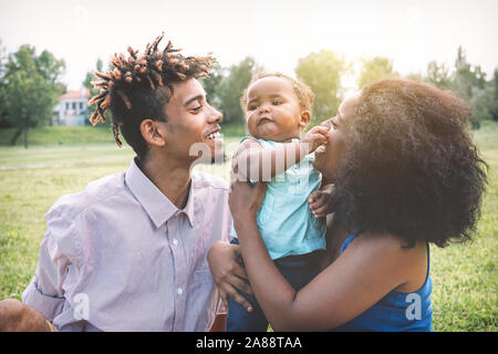 Happy black family enjoying a tender moment during the weekend outdoor - Mother and father having fun with their daughter in a public park