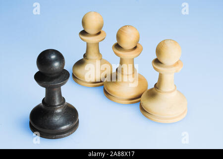 four chess pieces in front of a light blue coloured background. one black piece and three white pieces in a row. Stock Photo