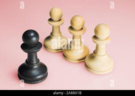 four chess pieces in front of a salmon-coloured background. one black piece and three white pieces in a row. Stock Photo