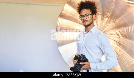 Self-confident young man as a photographer with camera in the photo studio Stock Photo