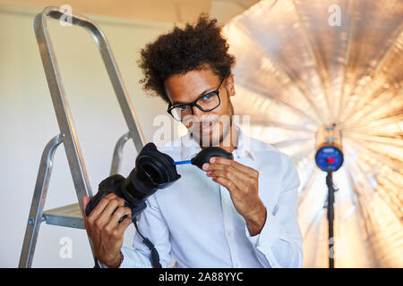 Young man as a photographer cleans camera lens with the bellows Stock Photo