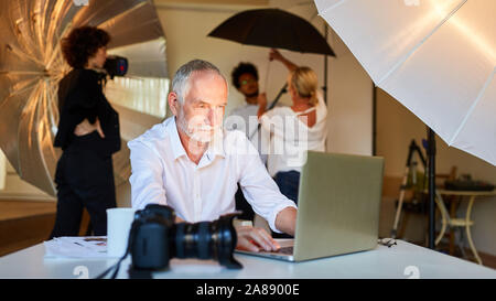 Photographer is working on pictures at laptop. Computer with team in background Stock Photo