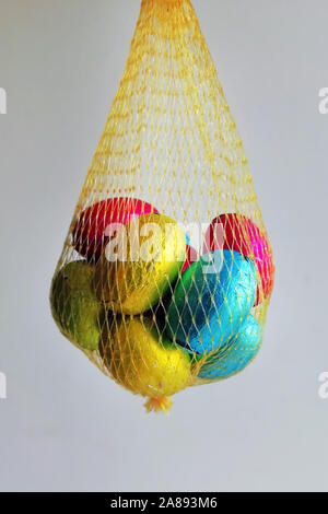 Multi colored eggs wrapped in foil folded into a yellow mesh. Chocolate eggs in a bag for children. Stock Photo
