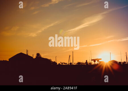 Sunset sun with rays over the track with silhouettes of buildings, wires and refueling Stock Photo