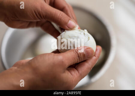 Indian housewife is peeling boiled eggs imperfectly in a bowl. Boiled peeled chicken eggs dish preparation concept. Stock Photo