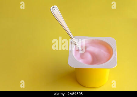Strawberrry pink yogurt in yellow plastic cup with spoon isolated on bright yellow background with space for text Stock Photo