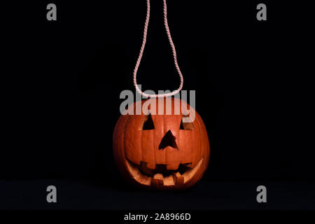 Pumpkin suspended on a rope. Preparation for Halloween.Orange squash on a black background with a white rope. Stock Photo