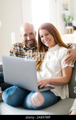 Smiling couple using laptop on sofa Stock Photo