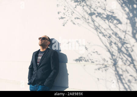 Man wearing sunglasses and blazer by white wall Stock Photo