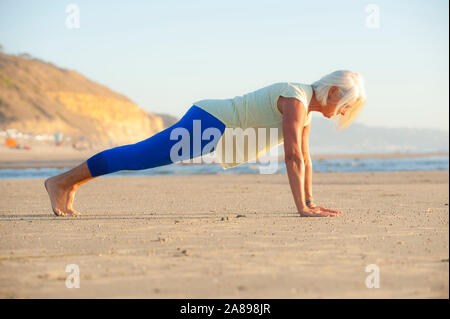 Mature woman doing push-ups on beach Stock Photo