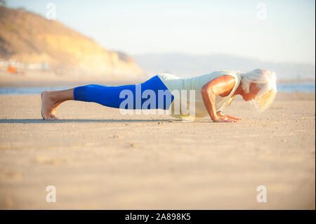 Mature woman doing push-ups on beach Stock Photo
